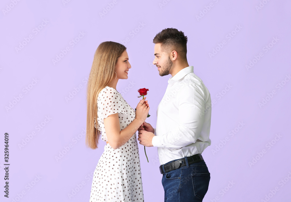Happy young couple with rose flower on color background