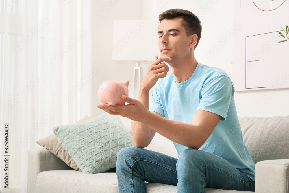 Thoughtful man with piggy bank at home