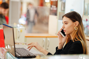 Wall Mural - Portrait of young caucasian female woman seller using laptop and orders goods by phone. Small business of candy souvenirs shop.