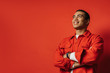 © Anton - Side view of positive arabian egyptian guy posing and smiling. Stand with hands crossed. Happy positive man isolated over red background.