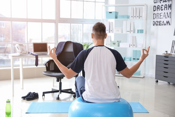 Wall Mural - Man meditating on fitness ball in office