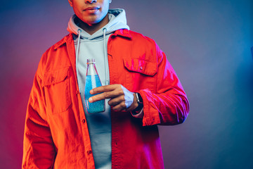 Wall Mural - Cut view of calm peaceful man stand alone and hold bottle with blue water in it. Arabian egyptian guy wear hoodie and red jacket. Cut view. Isolated over colorful background.