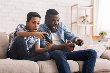 Wall Mural - Cheerful Black Father And Son Competing In Video Games At Home