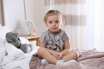 Wall Mural - Cute little girl sitting on bed at home