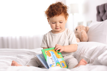 Sticker - Cute little child playing with book on bed at home