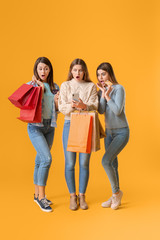 Sticker - Young women with mobile phone and shopping bags on color background