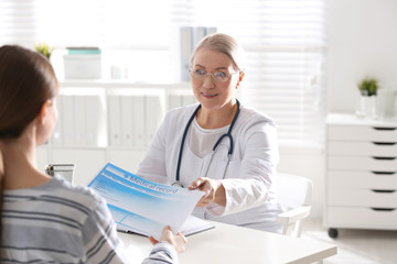 Doctor showing medical record to patient at desk in clinic