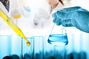 Wall Mural - hand of scientist holding flask and pouring sample to test tube with dropping yellow liquid to test tube in chemical laboratory background, science laboratory research and development concept