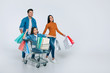 © My Ocean studio - Having fun. Full-length photo of three happy family members, who are enjoying their time together in a shopping center, carrying a lot of multicolored paper bags and riding a small child in a cart.