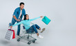 © My Ocean studio - Partners in crime. Full-length photo of a happy man in denim outfit pushing a shopping cart with an excited woman, who is holding paper bags in her spread arms, inside.