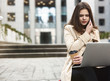 © studioprodakshn - young beautiful businesswoman works in her laptop drinks coffee sitting on stairs near office center in downtown, looks upset, multitasking concept