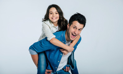 Happiness forever. Close-up photo of a happy family of a cute child and her happy dad, who is giving her a piggyback ride and laughing, while looking in the camera.