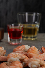 Close up boiled king prawns on a black plate with, standing on the kitchen table against the background of glasses with alcohol drinks. alcoholertical.