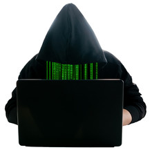 A Faceless Hacker In A Black Hoodie Sits At A Laptop. Instead Of A Face, A Green Binary Code. Front View.
