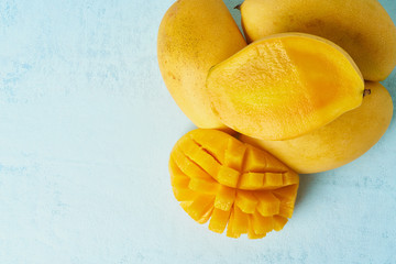 Four whole mango fruits on bright blue table and cut into slices. Large juicy yellow fruits