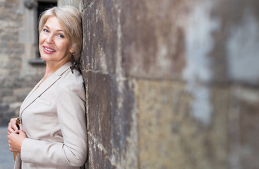 Wall Mural - Elegant mature woman is posing near old wall