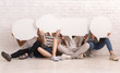 © Prostock-studio - Friends sitting on floor, hiding behind communication bubbles