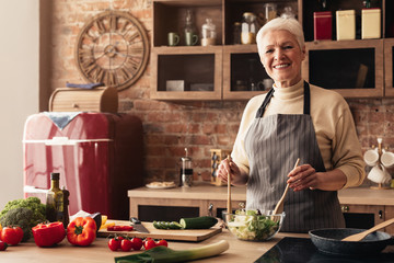 Happy Senior Woman Cooking Fresh Vegetable Salad And Looking At Camera