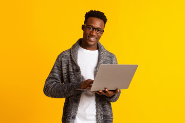 Handsome young african man using laptop on yellow