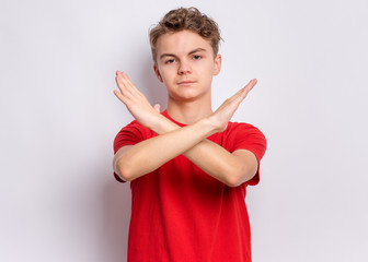 Wall Mural - Portrait of teen boy doing stop sign with crossed hands, on grey background. Cute caucasian young teenager making stop gesture with serious facial expression. Child looking at camera.