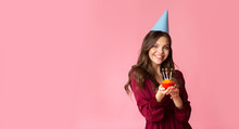 Joyful young girl holding cupcake with candles on birthday celebration party