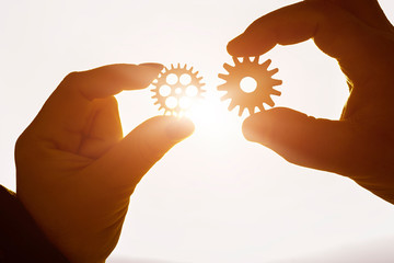 Two gears in the hands of people in the sun. The concept of interaction, the teeth mechanism.