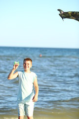  handsome boy in shorts and a t-shirt teenager launches a kite on the sky on the seashore in summer