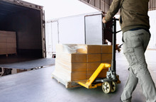 Workers Using Hand Pallet Jack Unloading Package Boxes Into Cargo Container. Delivery Shipment Boxes. Trucks Loading At Dock Warehouse. Supply Chain. Warehouse Shipping Transport And Logistics.