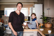 © Maskot - Portrait of smiling mature man with cup while daughter sitting on kitchen counter