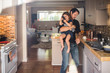 © Maskot - Daughter using phone while father carrying and working in kitchen