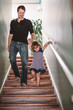 © Maskot - Smiling father holding hands of his daughter while walking downstairs at home