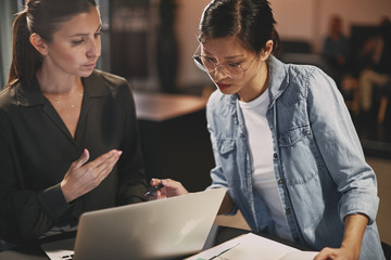 Wall Mural - Diverse businesswomen talking together over a laptop in an offic