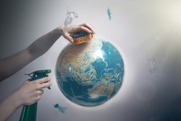 woman's hand holding a sponge and spray to clear the planet earth. the concept of improving the stat