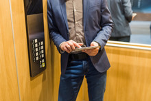 Man Hands Holding Tablet Device Next To Elevator Control Panel.