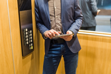 Man hands holding tablet device next to elevator control panel.