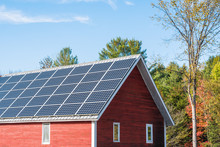 Solar Panels On The Roof Of A Red Wooden Barn On A Sunny Autumn Day. Concept Of Alternative Energy. Countryside Of Vermont, USA.
