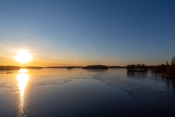 Wall Mural - Wintry landscape during sunset in Finland. Cold afternoon in February. Golden hour and reflecting ice and water on the shore.