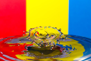 Abstract photograph of a water drop collision created with two water drops splashing together isolated against a red, yellow and blue background.