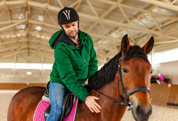 man jockey sitting on horse, horseback training on manege, lesson for jockey in equestrian school or