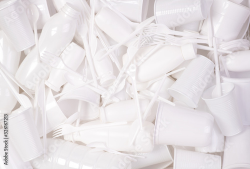 Disposable white single use plastic objects such as bottles, cups, forks and spoons that cause pollution of the environment, especially oceans. Top view.