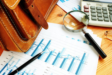 Auditing concept. Vintage briefcase and magnifying glass on the financial company papers.