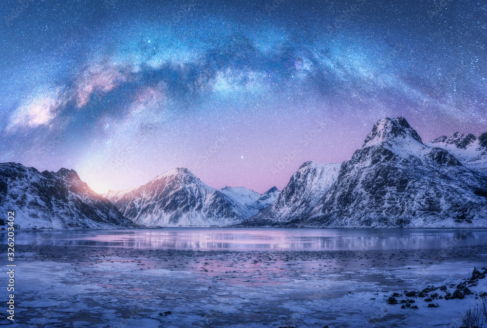 Milky Way above frozen sea coast and snow covered mountains in winter at night in Lofoten Islands, Norway. Arctic landscape with blue starry sky,  water, ice, snowy rocks, milky way. Space and galaxy - obrazy, fototapety, plakaty 
