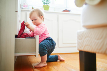 Wall Mural - Adorable toddler girl at home, opening the drawer of dresser and taking out clothes