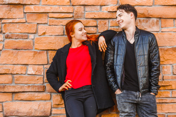 A young man and a girl stand with their backs to a stone wall