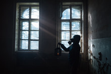 Dramatic Portrait Of A Female Wearing A Gas Mask At A Window With Sun Rays Symbolizing Hope In A Ruined Building.