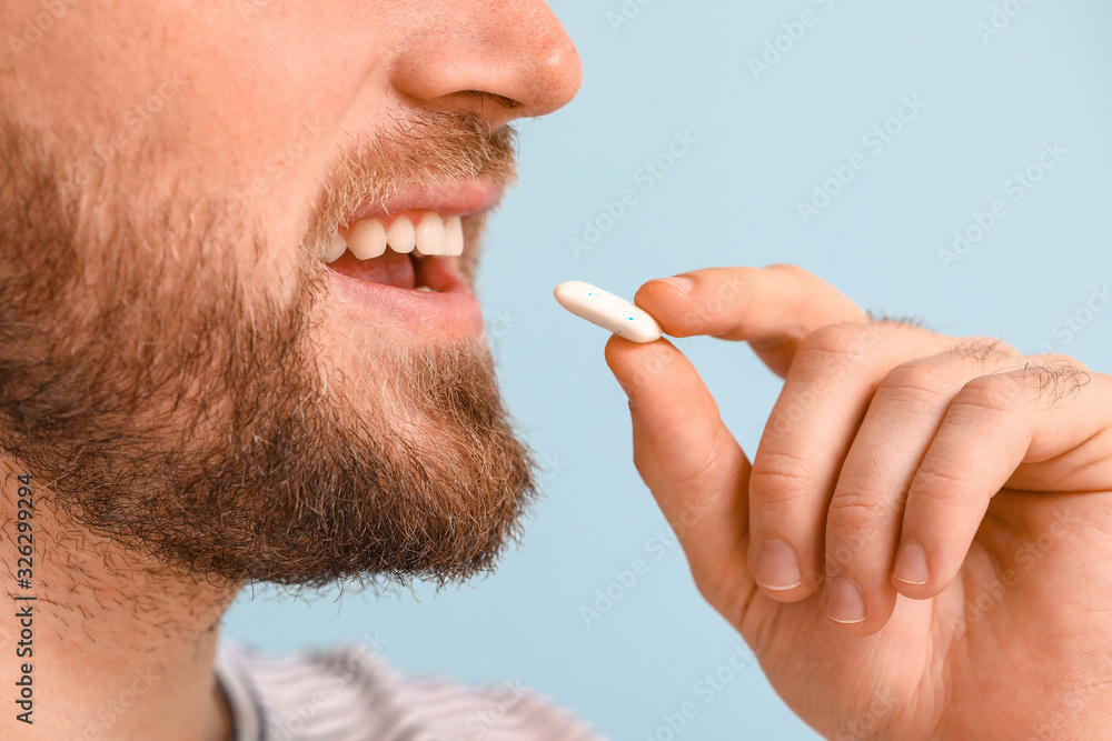 Young man with chewing gum on color background, closeup