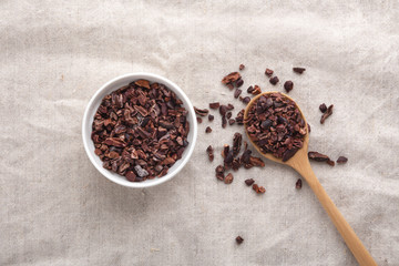 Cacao nibs in white bowl and wooden spoon on table