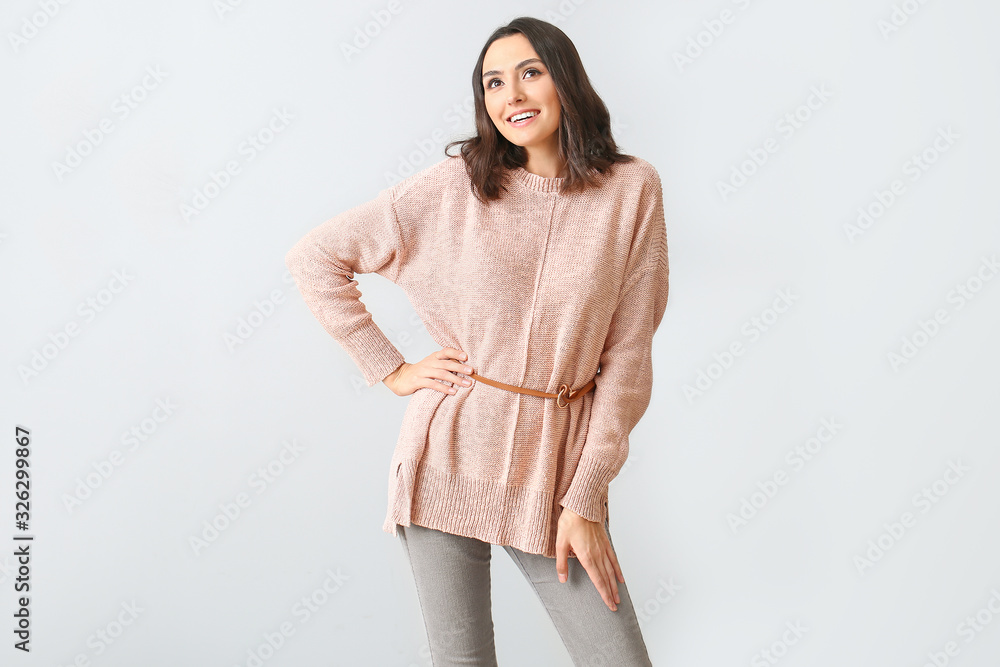 Beautiful young woman in warm sweater on light background