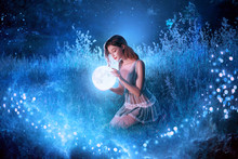 Fairytale Sorceress Holds In Hands Magical Ball Planet Universe Space Sitting In Night Forest. Goddess With Long Red Hair In Short Sexy Blue Dress. Backdrop Flying Bright Sparkle Stars White Grass Fog
