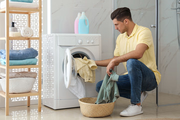 Poster - Man putting clothes into washing machine in bathroom. Laundry day